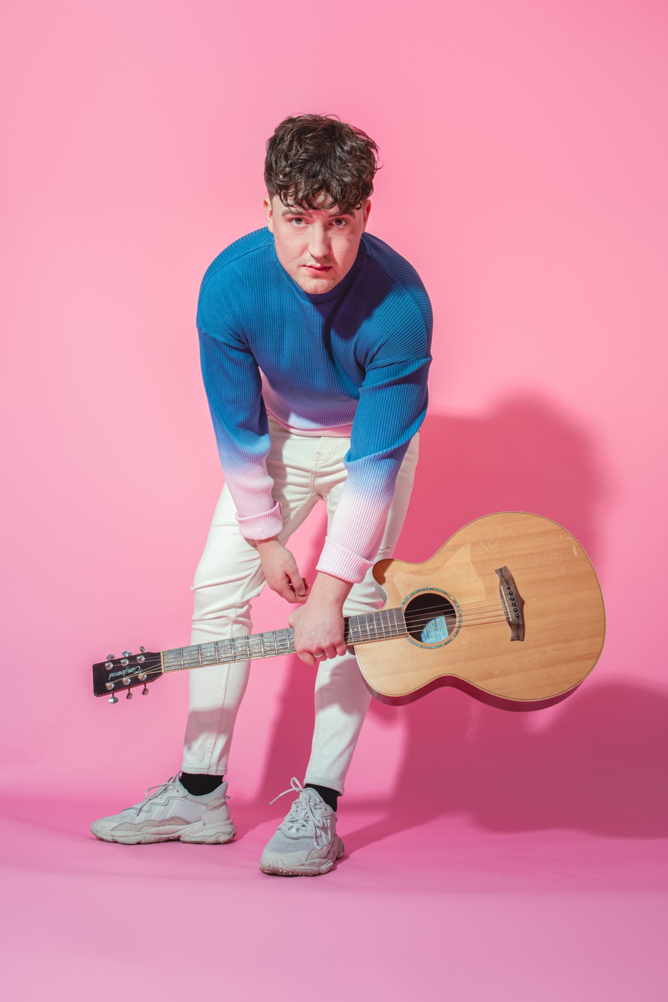 Musician holding an acoustic guitar against a pink studio background
